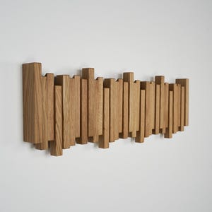 May include: A wooden wall-mounted coat rack with a series of vertical and horizontal wooden pieces. The rack is made of light brown wood and is mounted on a white wall. The design is modern and minimalist.