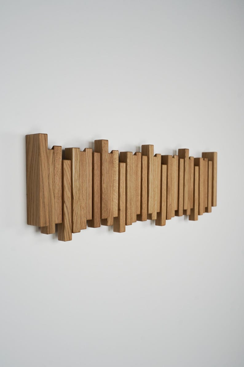 May include: A wooden wall-mounted coat rack with a series of vertical and horizontal wooden pieces. The rack is made of light brown wood and is mounted on a white wall. The design is modern and minimalist.