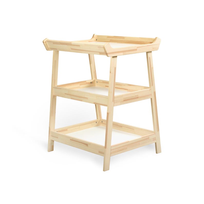 May include: A light-colored wooden changing table with two shelves and a top surface. The changing table has a simple, modern design with a rectangular shape and rounded edges. The shelves have white inserts.