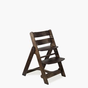 May include: A dark brown wooden high chair with a stepped design. The chair has a seat and footrest, and a backrest with horizontal slats. The chair is designed for a child and is made of wood.