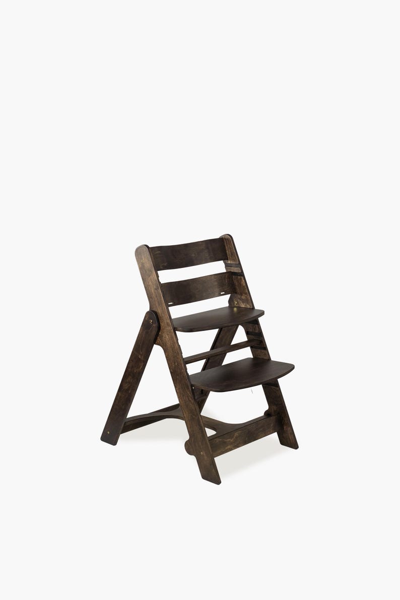 May include: A dark brown wooden high chair with a stepped design. The chair has a seat and footrest, and a backrest with horizontal slats. The chair is designed for a child and is made of wood.