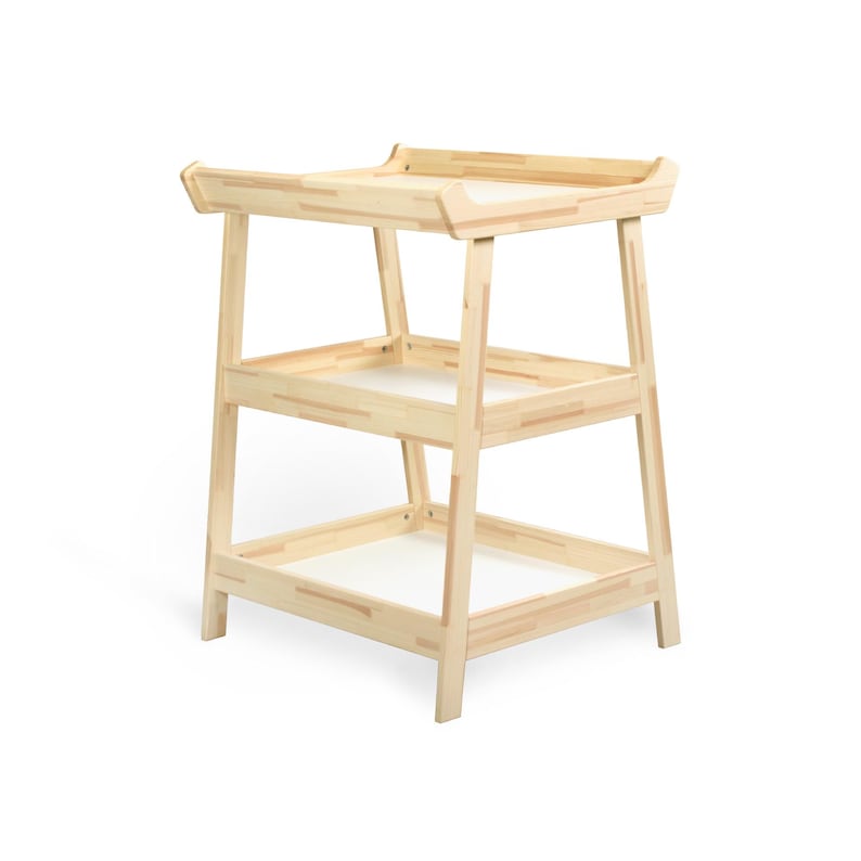 May include: A light-coloured wooden changing table with two shelves and a top surface. The changing table has a simple, modern design with a rectangular shape and rounded edges. The shelves have white inserts.