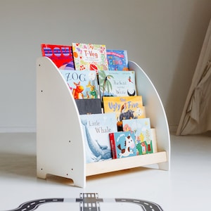 May include: White wooden bookshelf with rounded edges, holding a collection of colourful children's books. The books have titles like "Zog", "The Swish of the Whistle", "The Ugly Five", and "Little Whale".
