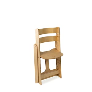 May include: A light-colored wooden folding chair. The chair has a curved backrest with three horizontal slats. The seat is a rounded rectangle. The chair is designed to fold for storage. The wood has a natural finish.