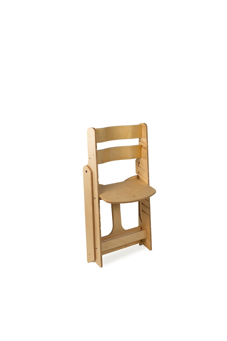 May include: A light-colored wooden folding chair. The chair has a curved backrest with three horizontal slats. The seat is a rounded rectangle. The chair is designed to fold for storage. The wood has a natural finish.