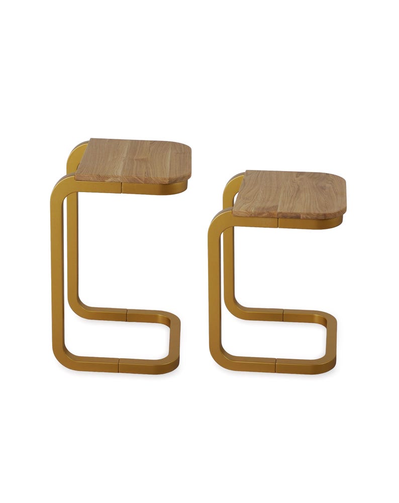 Op de afbeelding: Twee bijzettafels met een modern design. Elke tafel heeft een lichtgekleurd, rechthoekig houten blad en een goudkleurig, gebogen metalen frame. De tafels worden tegen een witte achtergrond getoond.