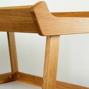 May include: Close-up of a wooden chair with a light brown finish. The chair has a curved backrest and angled legs, showcasing a minimalist design. The wood grain is visible, adding texture to the piece. The chair appears sturdy and well-crafted.
