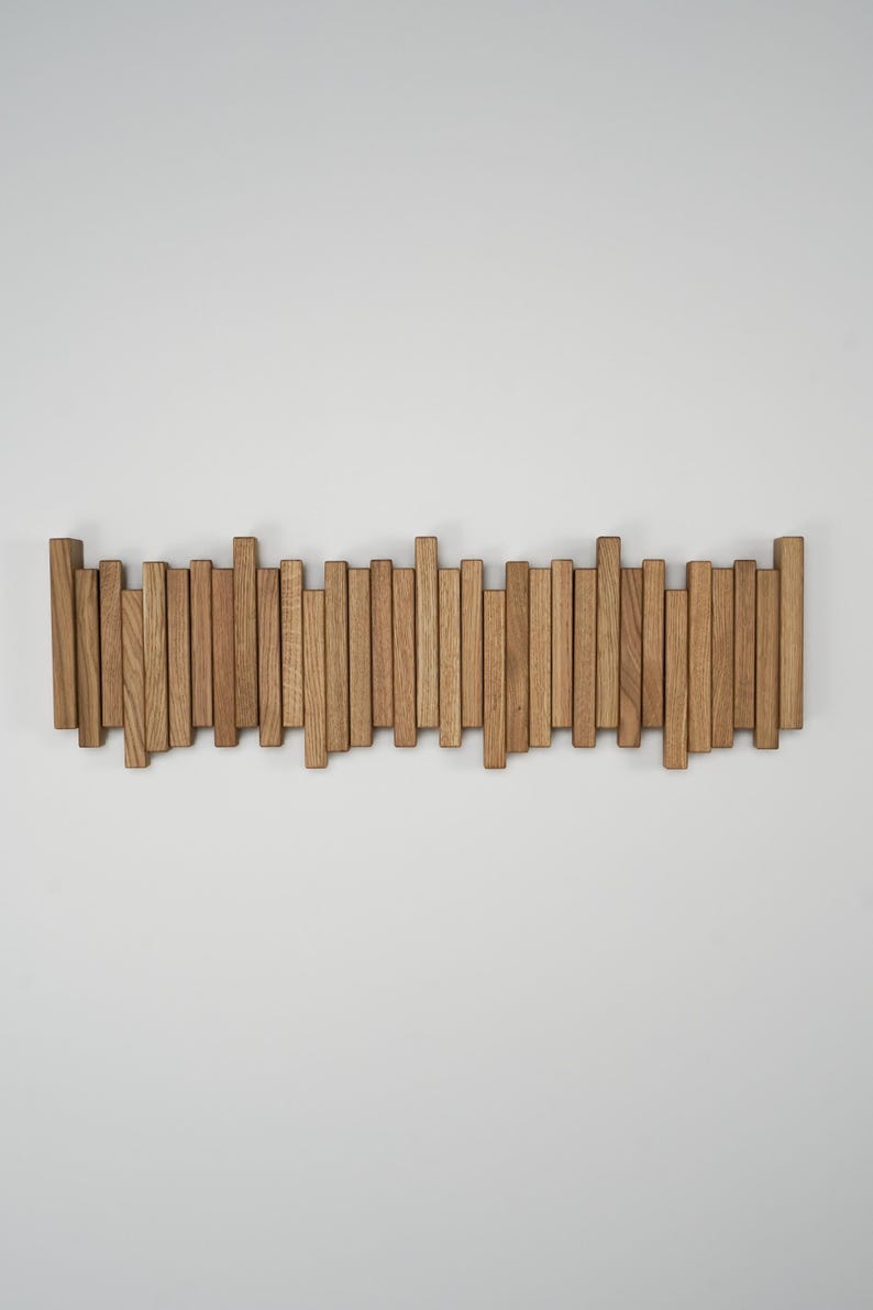 May include: A wooden wall-mounted coat rack with a series of vertical wooden slats of varying heights. The natural wood has a light brown color and is mounted on a white wall. The rack is designed for hanging coats or other items.