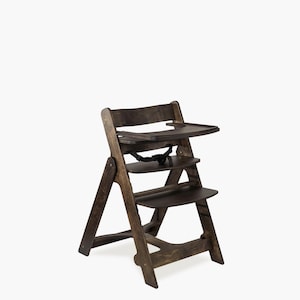 May include: A wooden high chair with a dark brown finish. The chair has a tray, a seat, and a footrest. It features a safety strap and is designed for a child. The chair is made of wood and has a simple, classic design.