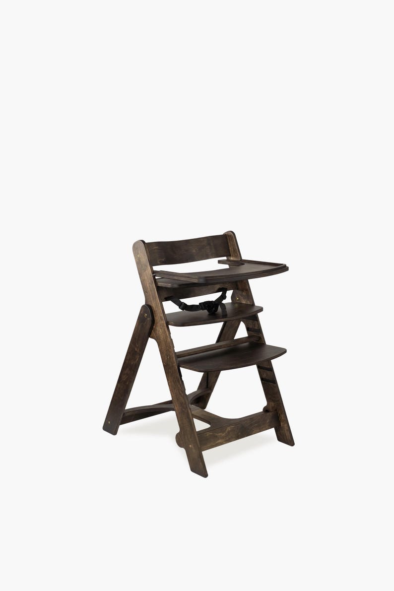 May include: A wooden high chair with a dark brown finish. The chair has a tray, a seat, and a footrest. It features a safety strap and is designed for a child. The chair is made of wood and has a simple, classic design.