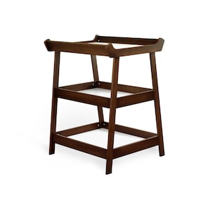 May include: A dark brown wooden changing table. It features a rectangular top with curved edges and two lower shelves. The legs are angled for stability. The design is simple and functional, suitable for a nursery. The measurements are in centimeters.