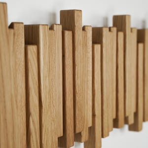 May include: A wooden wall art piece featuring a series of vertical, rectangular wooden blocks of varying heights. The blocks are arranged in a staggered pattern, creating a textured, three-dimensional effect. The wood has a natural, light brown color.