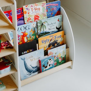 May include: A white wooden bookshelf with five shelves, each holding a different children's book. The books have colorful covers with illustrations of animals, including a dinosaur, a snail, a whale, and a horse. The bookshelf is made of wood and has a curved design.