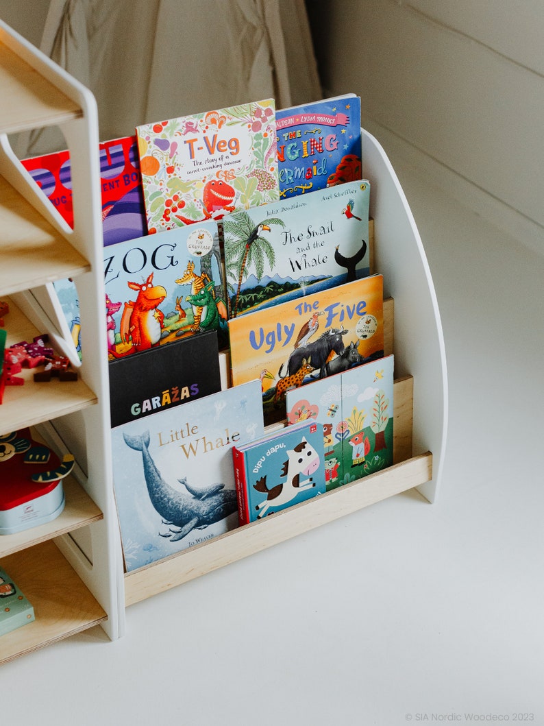May include: A white wooden bookshelf with five shelves, each holding a different children's book. The books have colorful covers with illustrations of animals, including a dinosaur, a snail, a whale, and a horse. The bookshelf is made of wood and has a curved design.
