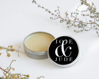 May include: A small tin container with a black lid featuring the text "JOE & JUDE" in white. The tin is open and contains a white balm.