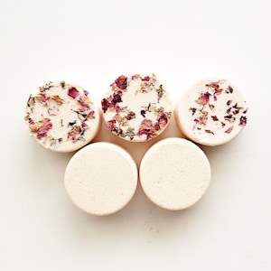 May include: Five round bath bombs with a white base and pink and white dried flowers embedded in the surface.