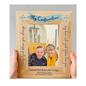 May include: A light-colored wooden picture frame with the words "My Confirmation" on a blue banner. The frame has blue crosses and text that reads "May God bless you always" and "and may angels guide you every day". The frame holds a photo of two people.