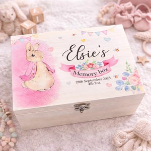 May include: A light-colored wooden memory box with a hinged lid. The box features a watercolor illustration of a bunny in a pink jacket, the name "Elsie's", and the text "Memory box". The box also includes the date "28th September 2025" and the weight "4lb 7oz".