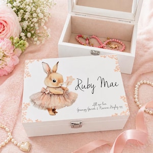 May include: A white wooden jewellery box with a hinged lid and a mirror inside. The box features a watercolour illustration of a bunny holding a star wand, the name "Ruby Mae", and the text "All our love".