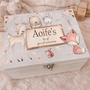 Op de afbeelding: Een witte houten herinneringsdoos met een lichtgrijs deksel met illustraties van bosdieren. Op het deksel staat de tekst "Aoife's box of special memories". Een hert, beer, konijn, vos en eekhoorn zijn afgebeeld.