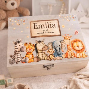 May include: A wooden memory box with a light blue lid. The lid features the name "Emilia" and the text "box of special memories." The box is decorated with cartoon animals: a zebra, tiger, horse, monkey, elephant, giraffe, and lion.