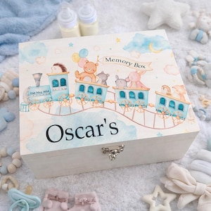 May include: A wooden memory box with a train illustration. The train cars are filled with cartoon animals and balloons. The box is light-colored with the name "Oscar's" and the date "21st May 2024" printed on it. A metal clasp secures the box.