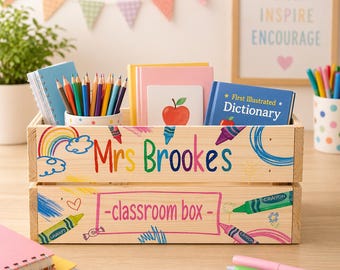 May include: A wooden classroom box, decorated with crayons and a rainbow, and the name "Mrs Brookes" in colourful letters. The box contains stationery, including pencils, notebooks, and a small dictionary. The words "-classroom box-" are also written on the box.
