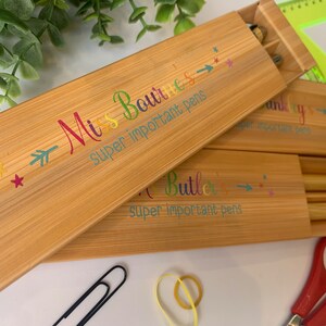 May include: Two wooden boxes with lids, each with a personalised inscription and two pens inside. The inscription on the top box reads "Miss Boutte's super important pens" and the inscription on the bottom box reads "A Butler's super important pens".