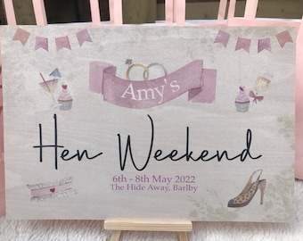 May include: A light pink and white sign with the text "Amy's Hen Weekend" and the dates "6th - 8th May 2022". The sign also includes the text "The Hide Away, Barlby".