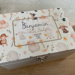 Può includere: Scatola portaoggetti in legno bianco con un design floreale e pecore. La scatola ha un coperchio incernierato con una chiusura argentata. La scatola è personalizzata con il nome "Benjamin Tobias Dowla", la data "24/09/2023", l'ora "21:26" e il peso "3,45 kg".