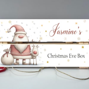 Puede incluir: Caja de Nochebuena de madera con un diseño festivo. La sección superior dice "Jasmine's" en una fuente cursiva. La sección inferior dice "Christmas Eve Box". Ilustraciones de Papá Noel y un reno.