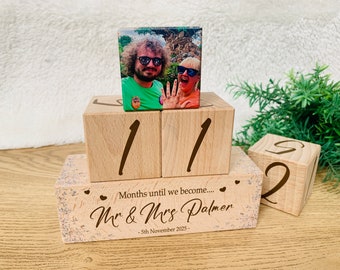 May include: Wooden block calendar with a photo of a couple on top. The calendar displays the numbers 11 and 2, with the text "Months until we become... Mr & Mrs Palmer - 5th November 2025" on the base. A unique wedding countdown.