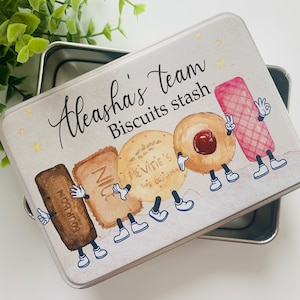 May include: A white metal tin with a colourful illustration of cartoon biscuits. The tin has the text "Aleasha's team Biscuits stash" on the front.