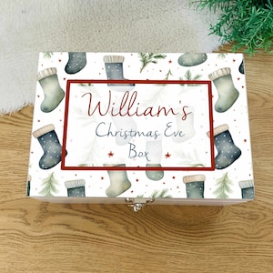 Puede incluir: Una caja de Nochebuena de madera con un diseño festivo. La caja presenta un patrón de calcetines navideños y abetos sobre un fondo blanco. El texto "William's Christmas Eve Box" se muestra en rojo y azul.
