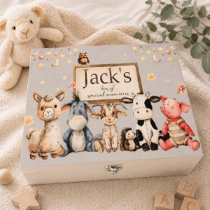 Peut inclure: Une boîte à souvenirs en bois avec un couvercle bleu clair orné d'illustrations d'animaux de la ferme et du texte "Jack's box of special memories". La boîte a un fermoir argenté et est entourée d'une couverture crème.