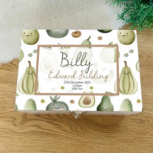 Könnte beinhalten: Eine weiße Holz-Erinnerungskiste mit einem grünen und braunen Avocado- und Birnenmuster. Die Kiste hat einen braunen Rahmen mit dem Text "Billy Edward Fielding 27. Dezember 2023 1:03 Uhr 10lb 5oz".