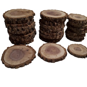 May include: A collection of wooden coasters made from tree slices. The coasters have a natural wood grain pattern and a rough bark edge. Several stacks of coasters are visible, along with individual coasters.