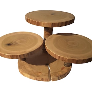 May include: A tiered wooden serving stand with three circular platforms of varying sizes. The natural wood has visible grain and a rough, unfinished edge. The stand is supported by a central trunk and smaller wooden supports.