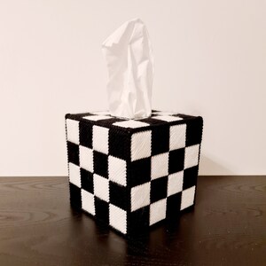 May include: A black and white checkered tissue box cover. The cover is made of fabric and has a square shape. A white tissue is sticking out of the top of the box.