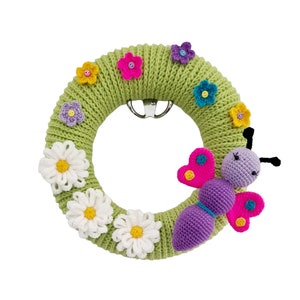Puede incluir: Una corona de crochet verde con una mariposa de crochet morado y flores de crochet de colores.