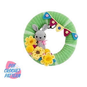May include: A green crocheted wreath with a gray bunny and yellow flowers. The wreath has a string of colorful flags around it.