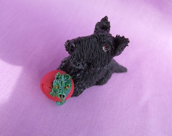 Puede incluir: Figura de un Terrier escocés negro con una bola roja con una cabeza de dragón verde. El perro tiene detalles de pelaje y ojos marrones. El dragón tiene ojos naranjas y emerge de la bola roja.