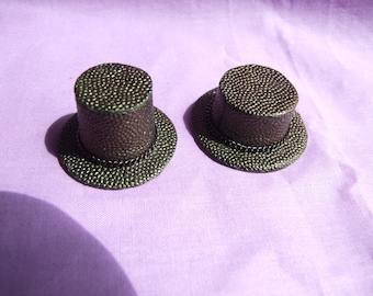 Puede incluir: Dos sombreros de copa en miniatura con un acabado texturizado verde oscuro. Los sombreros tienen una banda negra alrededor del borde.