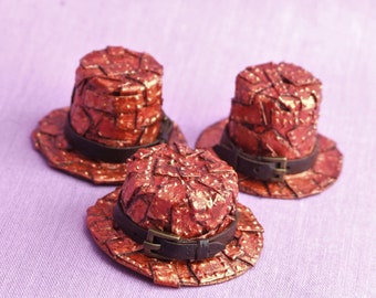 Puede incluir: Tres sombreros de copa en miniatura hechos de papel rojo con un diseño texturizado tipo mosaico. Cada sombrero tiene una banda de cuero marrón con una hebilla.
