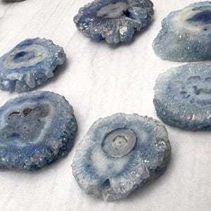 May include: A collection of blue and white geode slices. Each slice has a crystalline exterior and a contrasting center. The geodes vary in size and shape, with a range of blue hues.