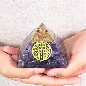 May include: A purple amethyst crystal pyramid with a gold flower of life design and a copper coil inside.