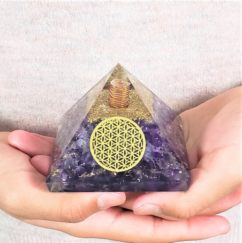 May include: A purple amethyst crystal pyramid with a gold flower of life design and a copper coil inside.