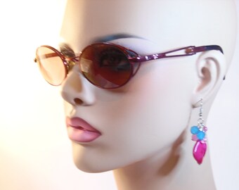 May include: A mannequin wearing burgundy oval sunglasses with brown lenses and pink and blue beaded earrings.