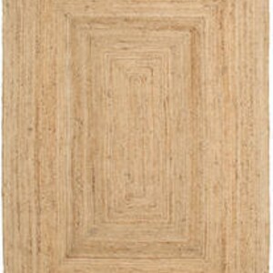 May include: Natural jute rug with a woven design featuring multiple concentric squares. The rug has a light brown color and a rectangular shape.