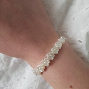 May include: A white bracelet made of small, pearl-like flower charms. The bracelet is on a person's wrist.